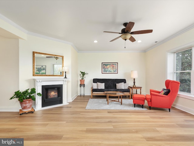 living room featuring light wood-type flooring, crown molding, recessed lighting, a glass covered fireplace, and baseboards