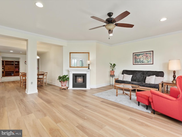 living room with ceiling fan, light wood-style floors, recessed lighting, ornamental molding, and a glass covered fireplace