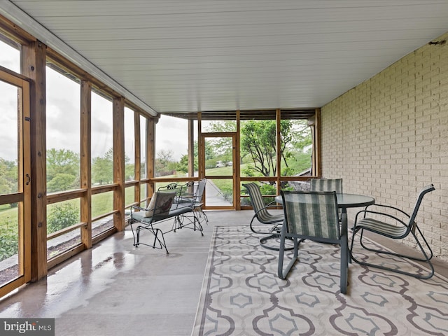sunroom featuring brick wall, outdoor dining space, floor to ceiling windows, and finished concrete floors