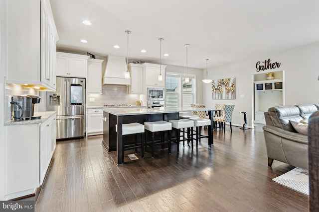 kitchen with premium range hood, stainless steel fridge, a kitchen breakfast bar, white cabinetry, and recessed lighting