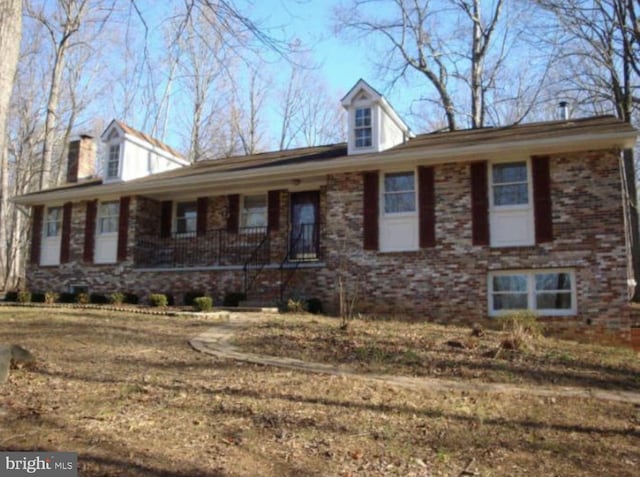 view of front facade featuring covered porch, brick siding, and a chimney