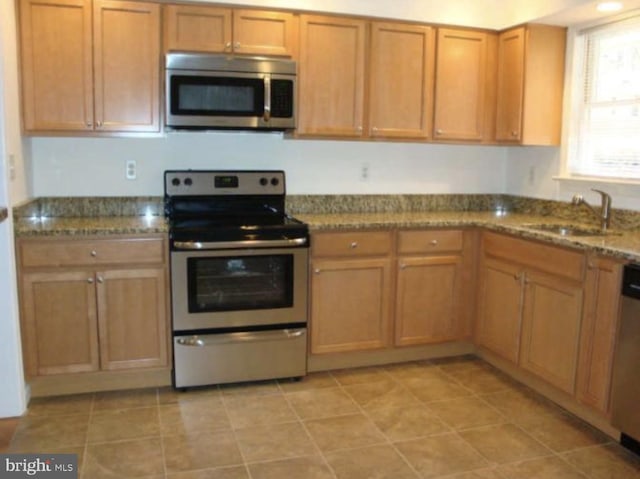 kitchen featuring stainless steel appliances, a sink, dark stone counters, and brown cabinets