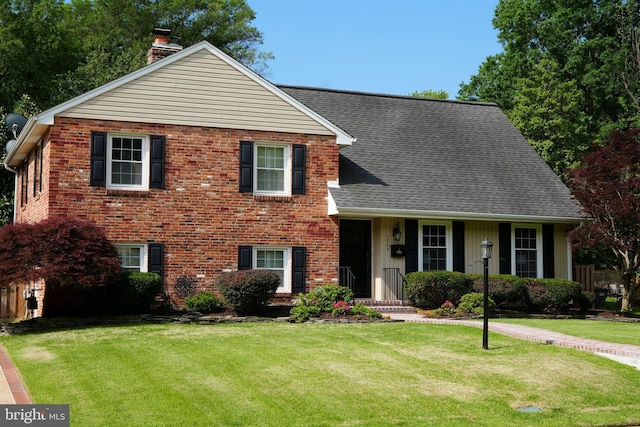 view of front facade featuring a chimney, a front lawn, roof with shingles, and brick siding