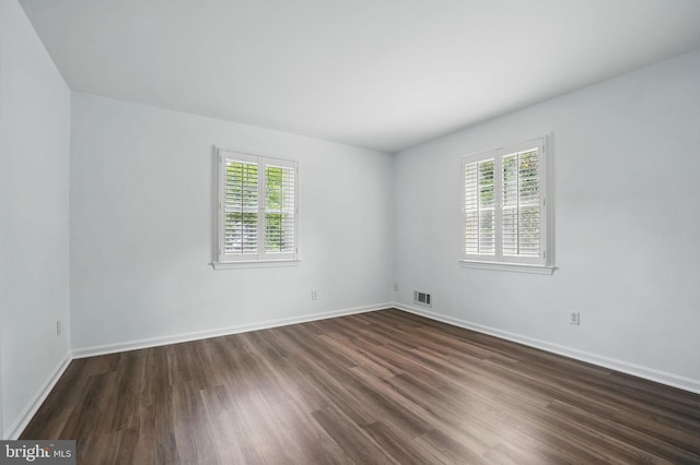 empty room featuring healthy amount of natural light, dark wood finished floors, and baseboards