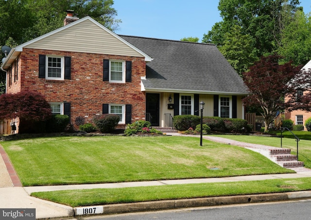 tri-level home with a chimney, a front lawn, brick siding, and roof with shingles