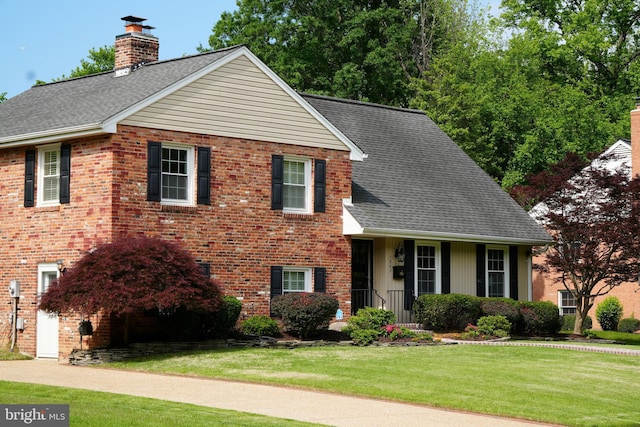 view of front of property with a chimney, a front lawn, brick siding, and a shingled roof