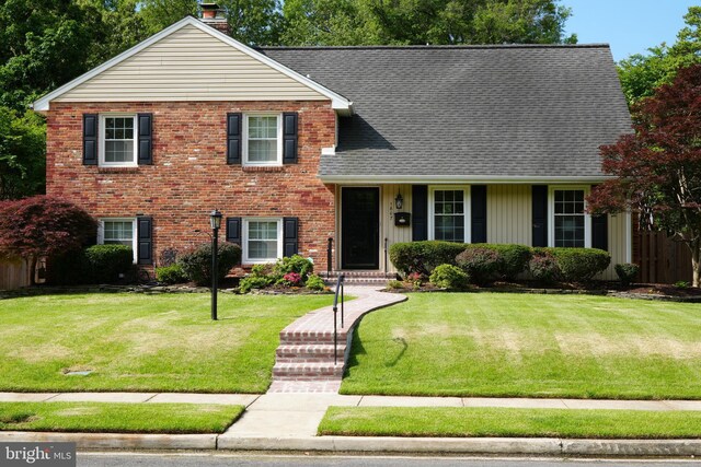 split level home with a front yard, a chimney, roof with shingles, and brick siding