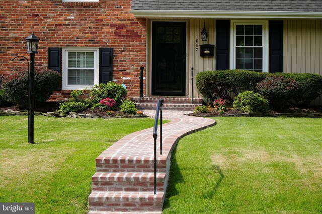 entrance to property with a shingled roof, a yard, and brick siding