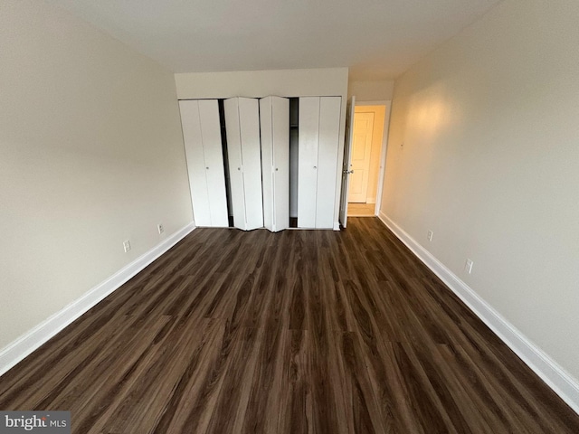 unfurnished bedroom with baseboards, dark wood-type flooring, and a closet
