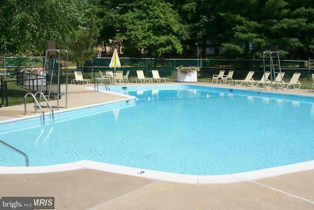 community pool featuring fence, a patio area, and view of wooded area