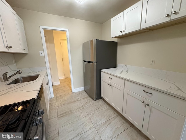 kitchen featuring a sink, gas range, light marble finish flooring, freestanding refrigerator, and white cabinetry