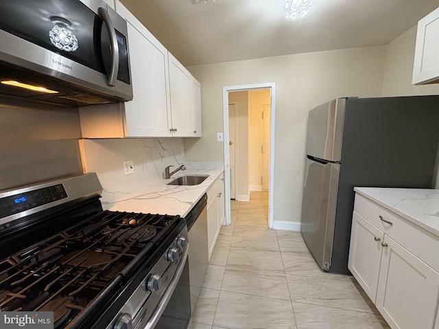 kitchen with stainless steel appliances, light marble finish flooring, white cabinets, a sink, and light stone countertops