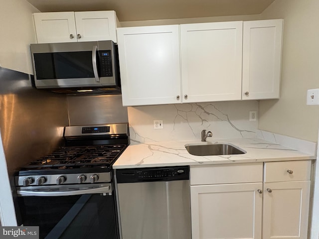 kitchen featuring appliances with stainless steel finishes, a sink, white cabinetry, and light stone countertops
