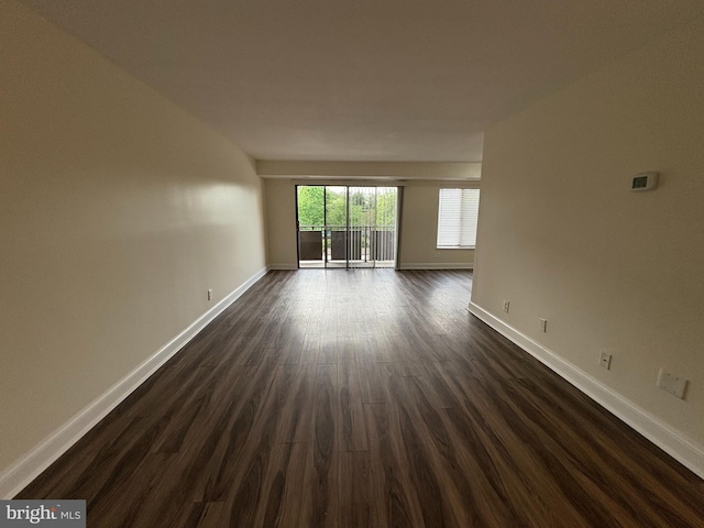 spare room with baseboards and dark wood-type flooring