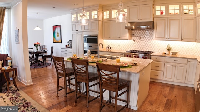 16 Magpie Ln, Princeton Junction, NJ 08550 - kitchen with under cabinet range hood, appliances with stainless steel finishes, light wood-style flooring, tasteful backsplash, and light stone counters