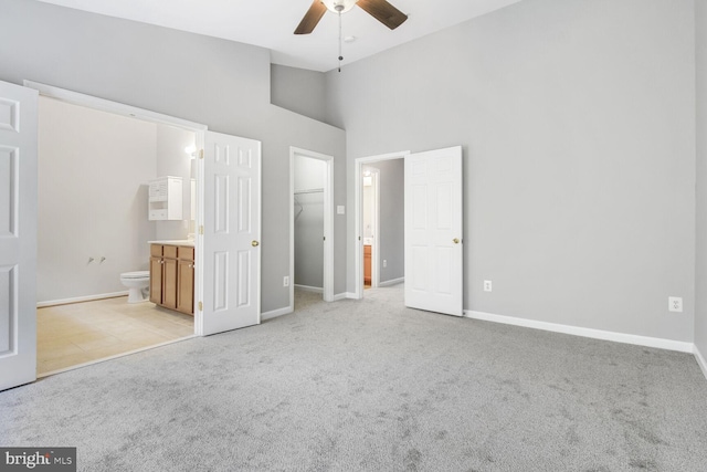 unfurnished bedroom with light carpet, a spacious closet, ensuite bathroom, baseboards, and high vaulted ceiling
