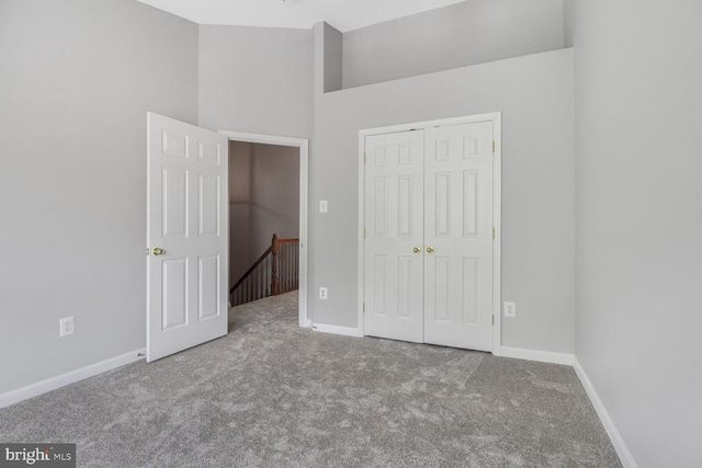 unfurnished bedroom with carpet flooring, baseboards, a closet, and a towering ceiling