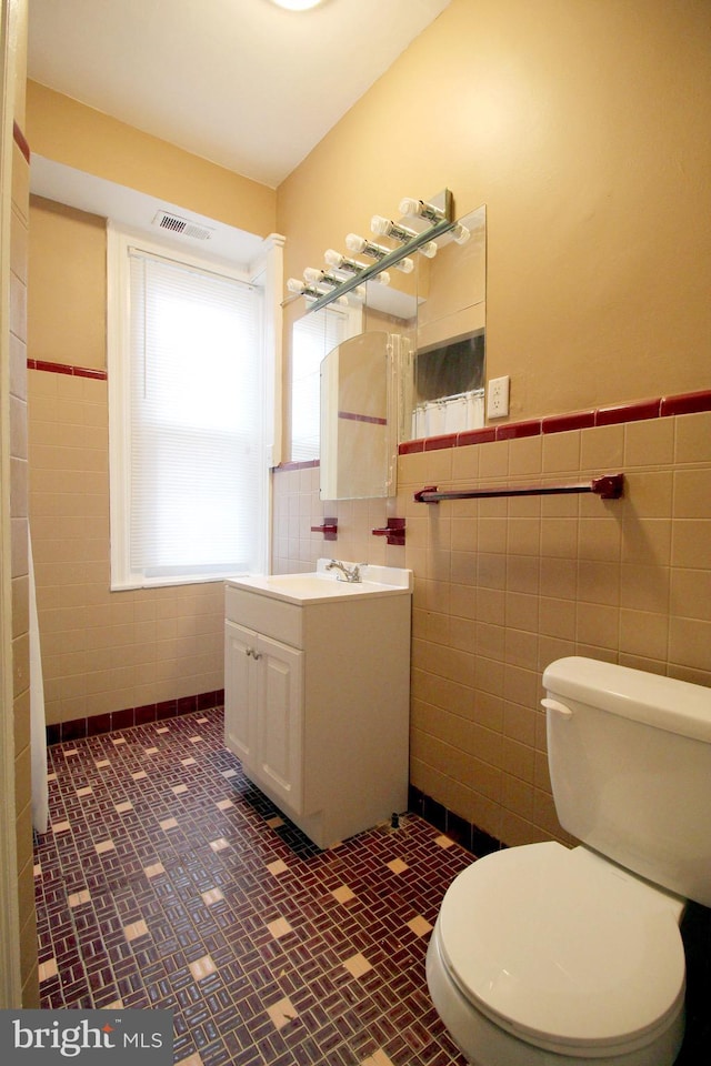 bathroom featuring tile walls, toilet, a wainscoted wall, and vanity