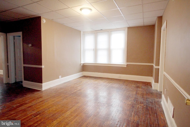 empty room featuring hardwood / wood-style flooring, a drop ceiling, and baseboards