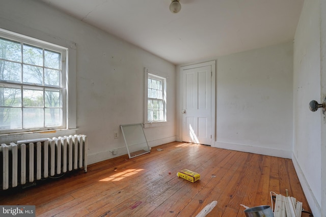 unfurnished bedroom featuring radiator heating unit, hardwood / wood-style flooring, and baseboards