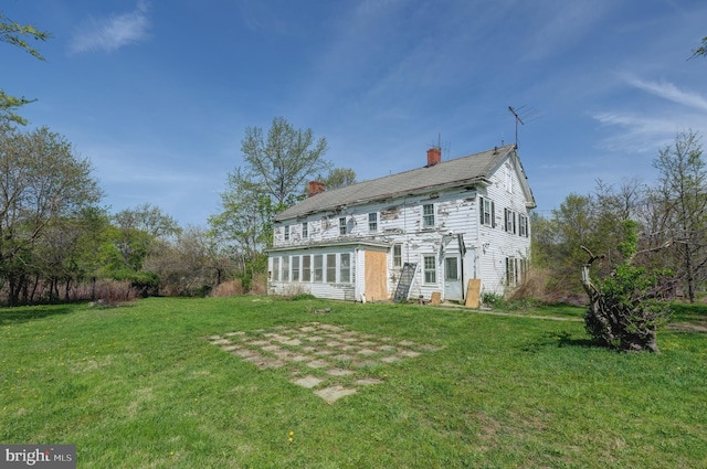 rear view of house featuring a chimney and a yard