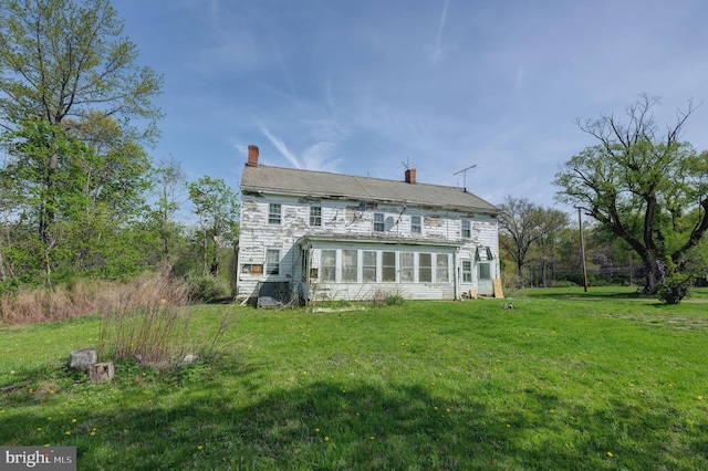 rear view of house with a chimney, a lawn, and a sunroom