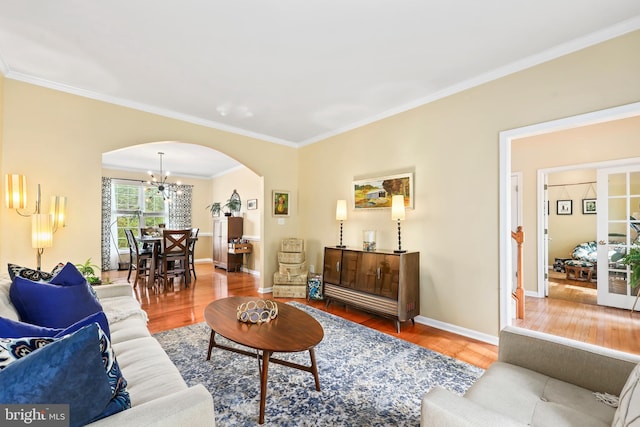 living room with arched walkways, ornamental molding, wood finished floors, a chandelier, and baseboards