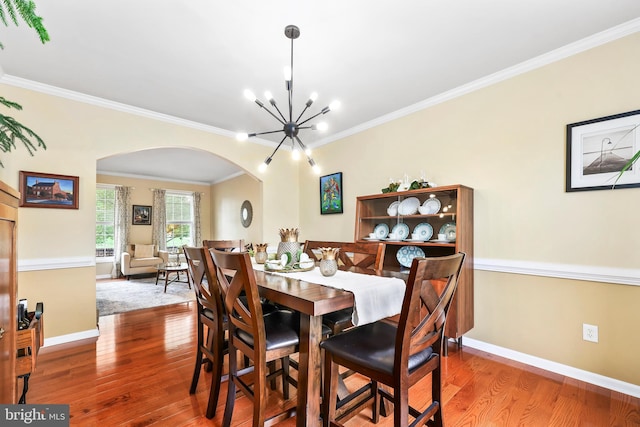 dining space featuring arched walkways, wood finished floors, a chandelier, ornamental molding, and baseboards