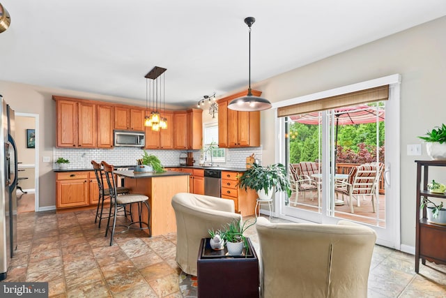 kitchen with appliances with stainless steel finishes, stone finish flooring, a center island, and tasteful backsplash