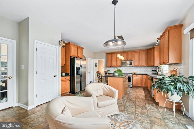 kitchen with appliances with stainless steel finishes, stone tile flooring, dark countertops, decorative backsplash, and baseboards