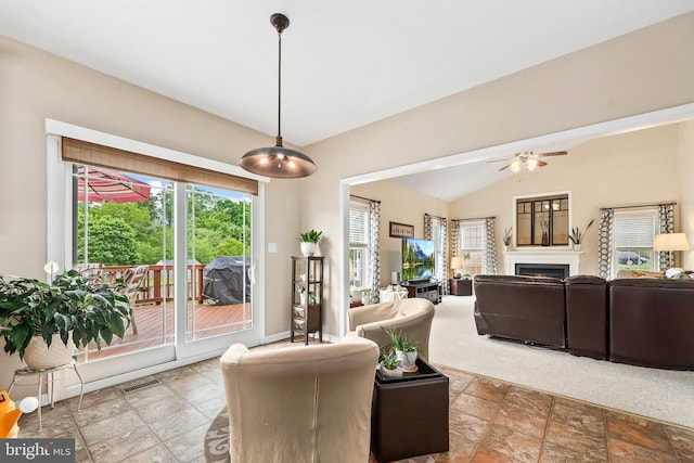 living room featuring stone tile floors, a fireplace, vaulted ceiling, a ceiling fan, and baseboards