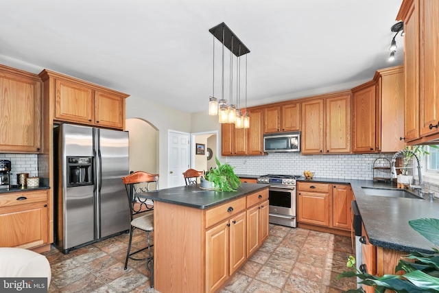 kitchen with appliances with stainless steel finishes, a sink, dark countertops, and stone finish flooring