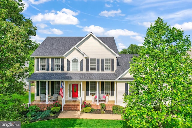colonial house featuring covered porch, a shingled roof, and a front lawn