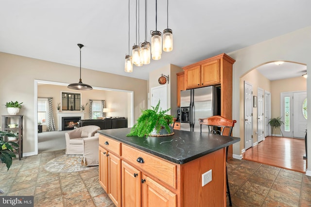 kitchen with stainless steel fridge with ice dispenser, arched walkways, stone tile floors, a center island, and baseboards