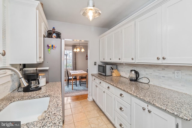 5100 Eugene Ave, Baltimore, MD 21206 - kitchen with stainless steel microwave, a sink, a chandelier, white cabinetry, and backsplash