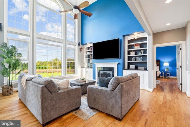 living area featuring a ceiling fan, plenty of natural light, a fireplace, light wood-type flooring, and a high ceiling