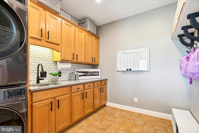 kitchen featuring stacked washer and clothes dryer, a sink, light countertops, baseboards, and decorative backsplash
