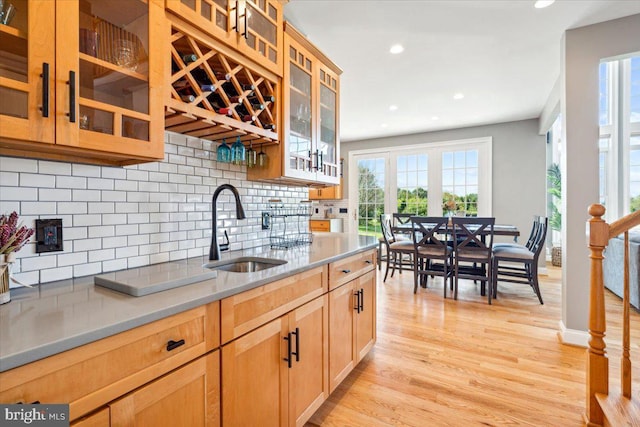 kitchen with a sink, backsplash, light wood-type flooring, recessed lighting, and glass insert cabinets