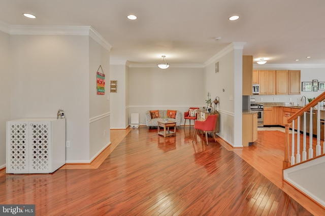 recreation room with light wood-style floors, ornamental molding, recessed lighting, baseboards, and a sink