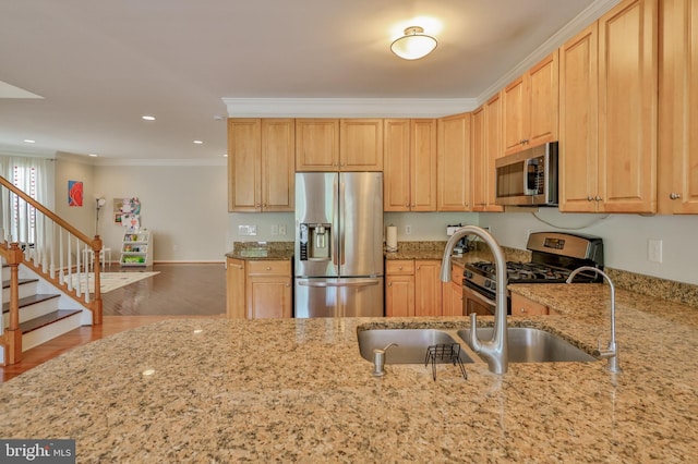 kitchen featuring stainless steel appliances, light stone countertops, crown molding, a sink, and light brown cabinets