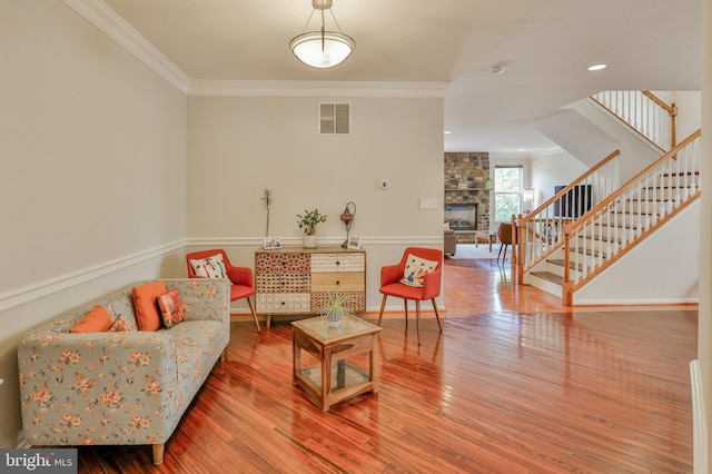 living area with ornamental molding, stairs, a stone fireplace, hardwood / wood-style floors, and baseboards