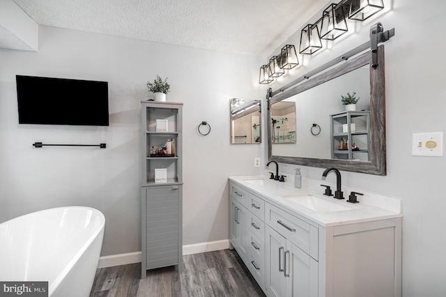 full bathroom featuring wood finished floors, double vanity, a soaking tub, a textured ceiling, and baseboards
