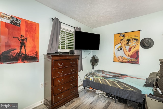 bedroom with wood finished floors, a textured ceiling, and baseboards