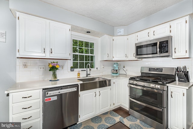 kitchen with appliances with stainless steel finishes, a sink, light countertops, decorative backsplash, and white cabinetry