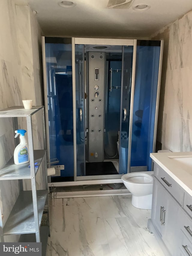 bathroom featuring marble look tile flooring, a stall shower, vanity, and toilet