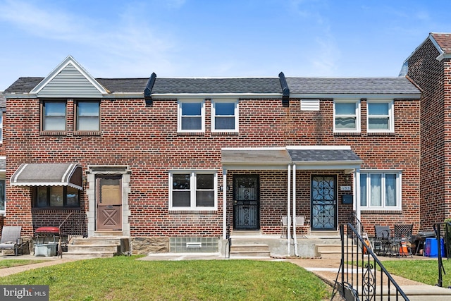 townhome / multi-family property featuring brick siding, a front yard, and roof with shingles