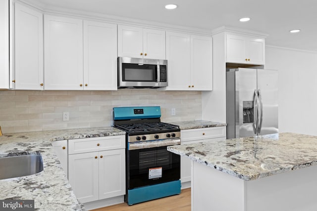 kitchen featuring appliances with stainless steel finishes, white cabinetry, light stone counters, light wood finished floors, and crown molding