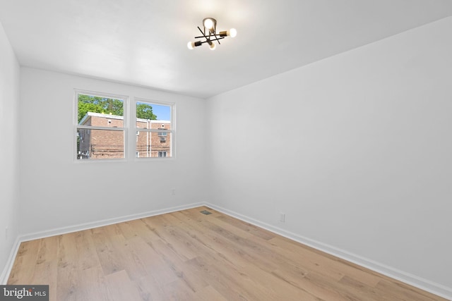 spare room with a chandelier, wood finished floors, and baseboards