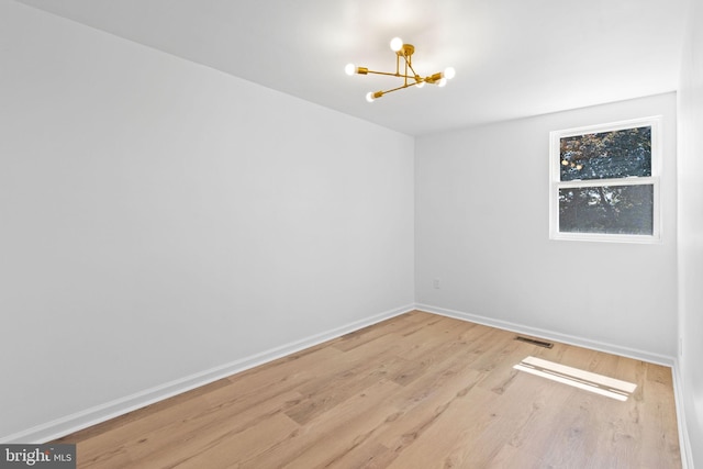 empty room featuring a chandelier, wood finished floors, and baseboards