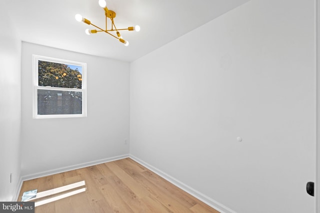 unfurnished room featuring a chandelier, light wood-style flooring, and baseboards